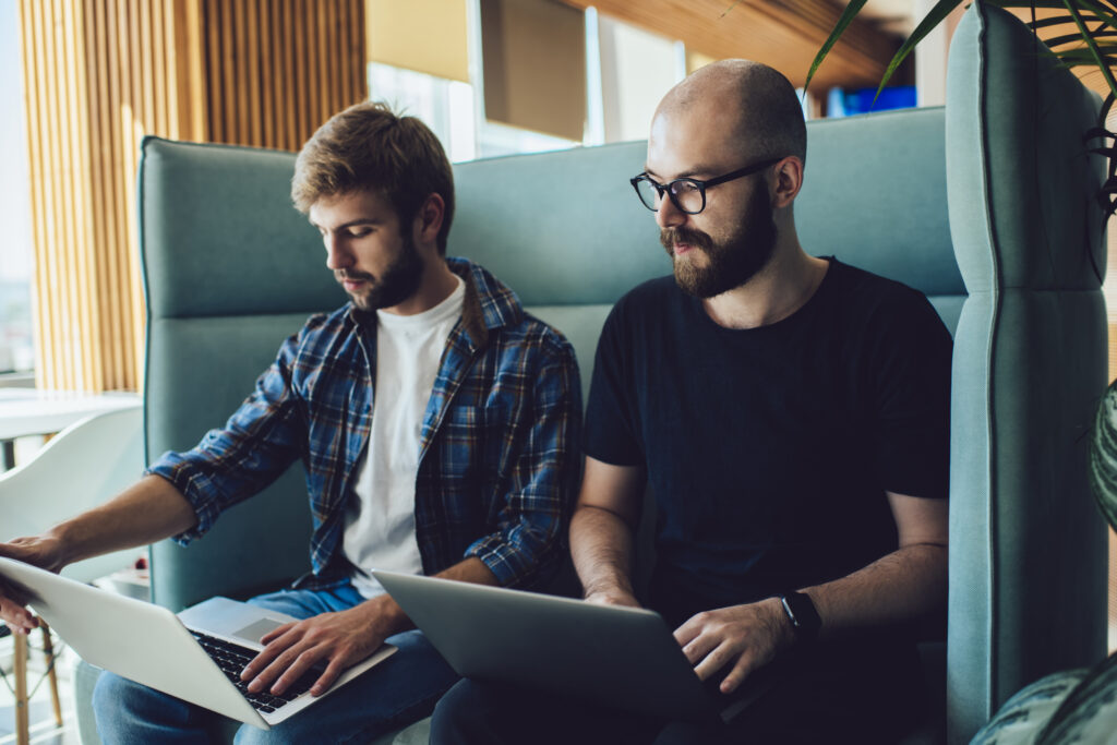 Two digital marketers analyzing Facebook ad performance on laptops in a modern office setting, focusing on reducing ad fatigue and improving ROI.